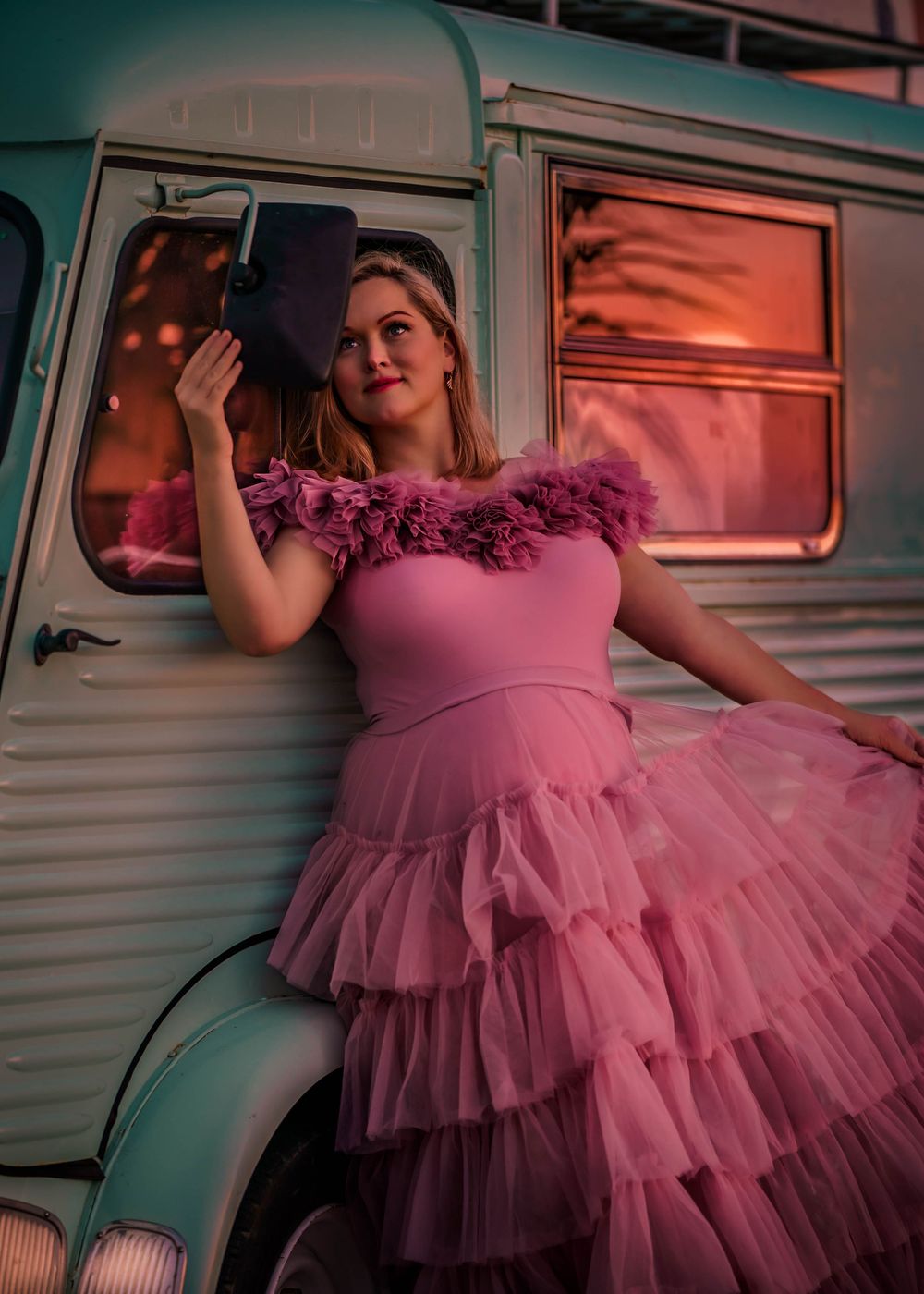 Maternity portrait with woman in pink dress leaning against turquoise vintage vehicle.