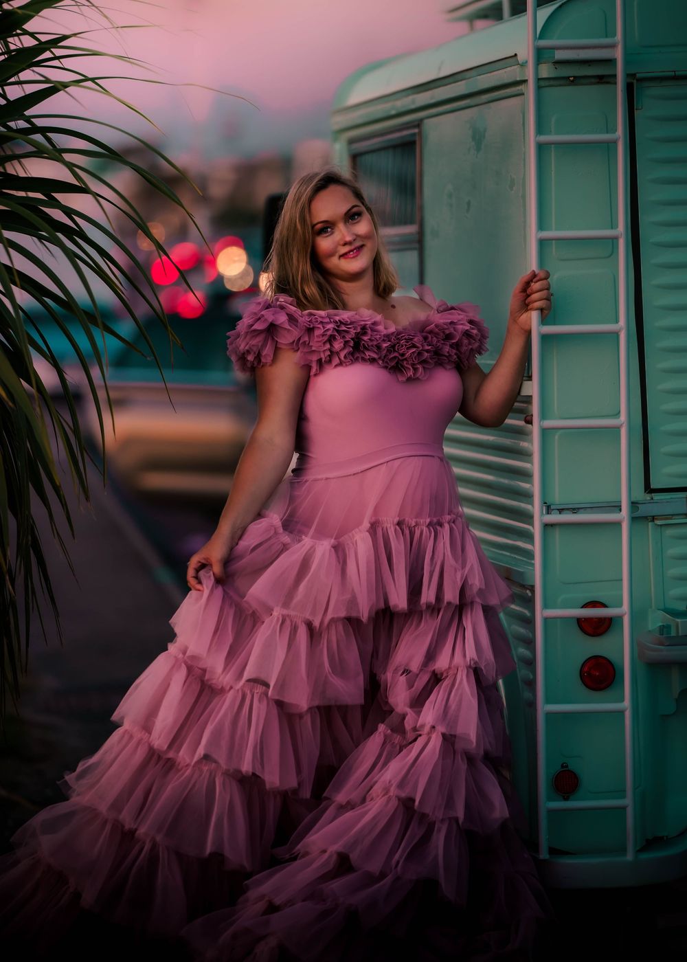 A pink layered tulle evening gown photographed against a turquoise building at sunset.