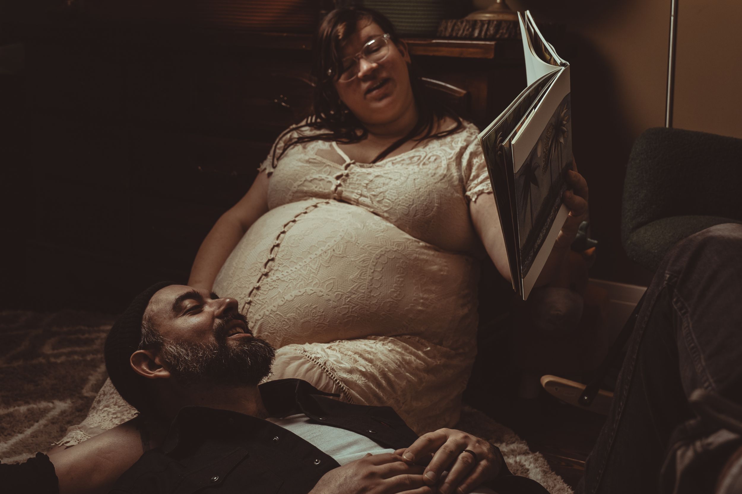 Couple expecting a baby share an intimate moment in a dimly lit room, with focus on the pregnant belly.