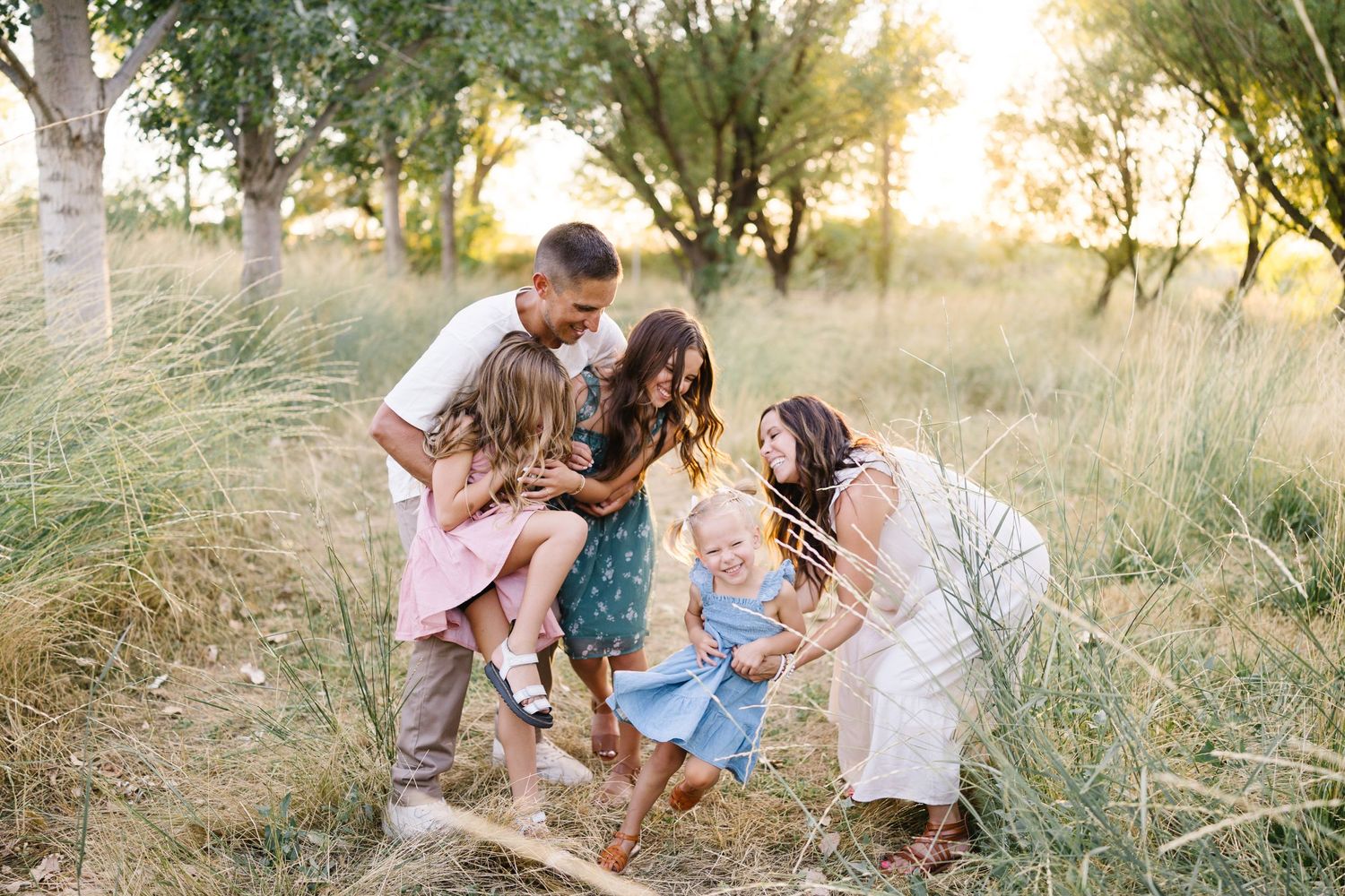 A joyful group plays together in a sun-drenched field with tall grass during golden hour.