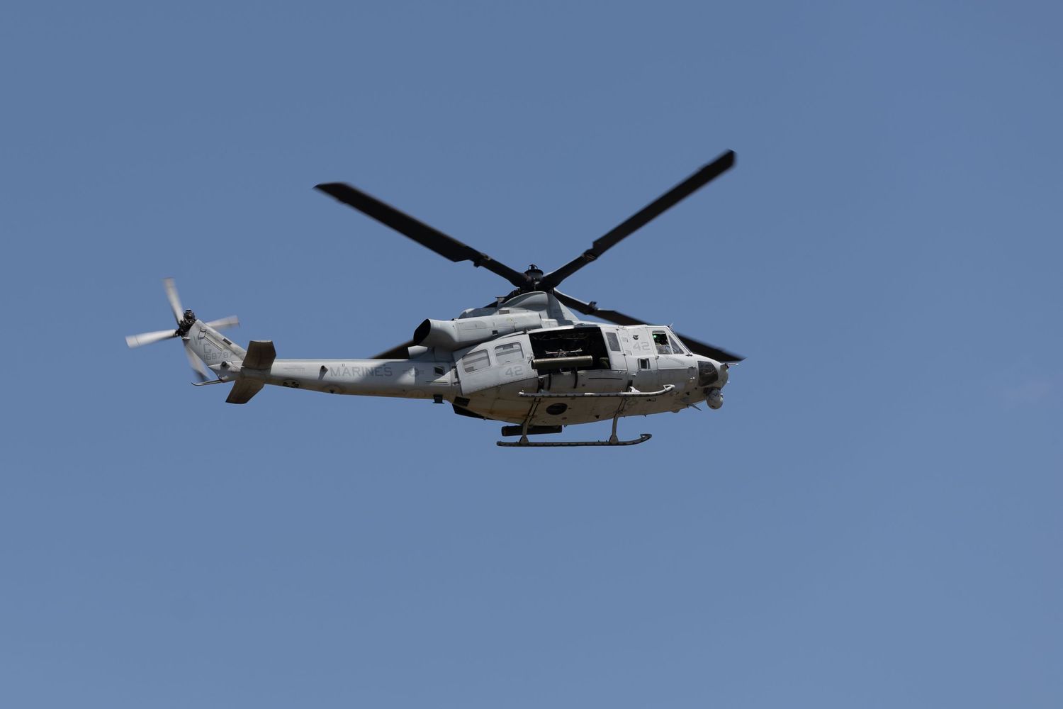 UH-1Y Venom military utility helicopter flying against bright blue sky during airshow.