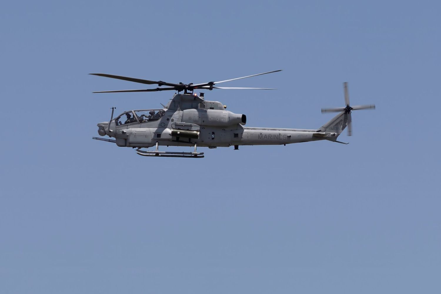 A USMC AH-1Z Viper attack helicopter flying against clear blue sky during military demonstration.