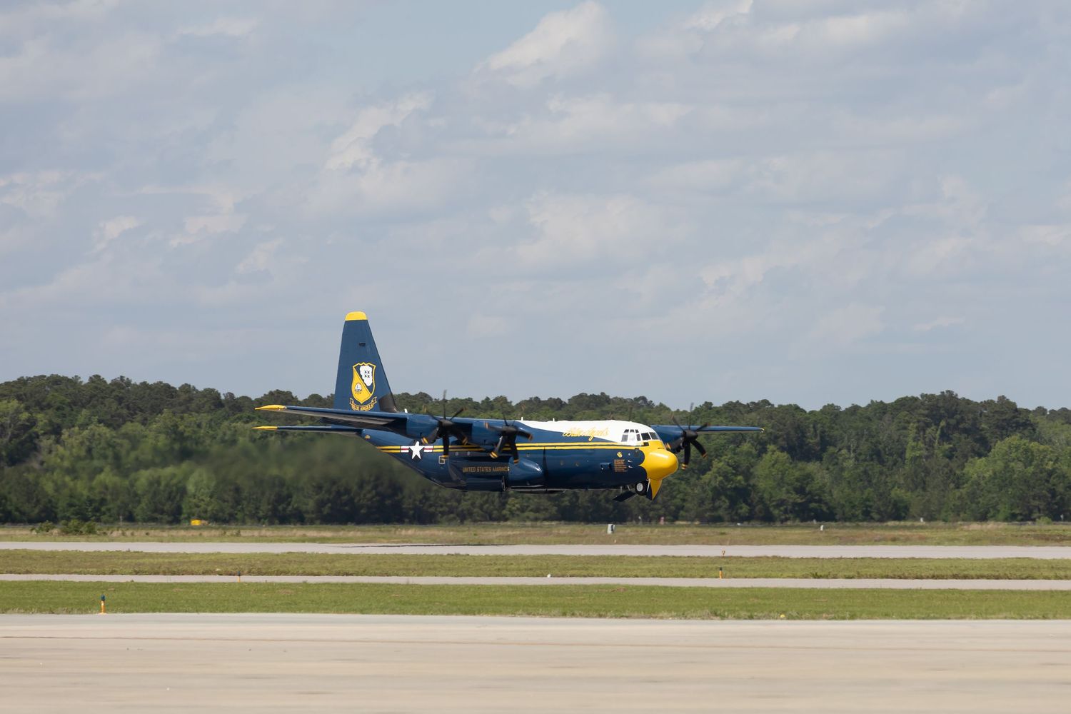 Blue and yellow C-130 Fat Albert aircraft landing on runway during airshow demonstration.