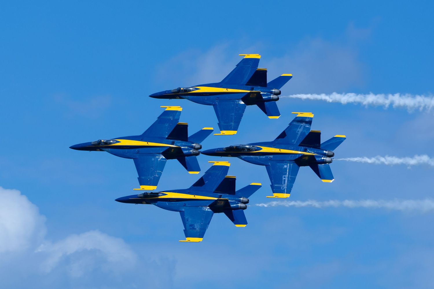 Blue Angels jets performing precision flight demonstration in diamond formation with white smoke trails.