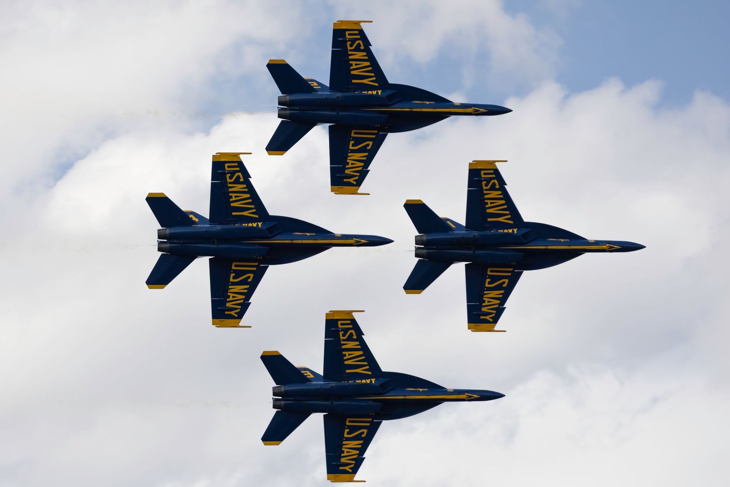 Four Blue Angels jets flying in tight diamond formation against cloudy sky during an airshow performance.