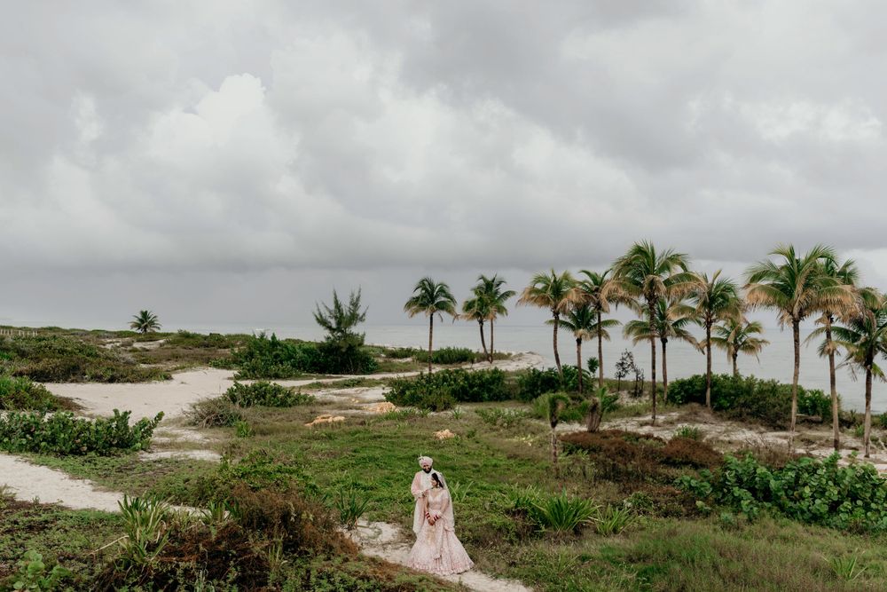 A lone figure walks along a winding path with palm trees and cloudy skies at a tropical coastal location.