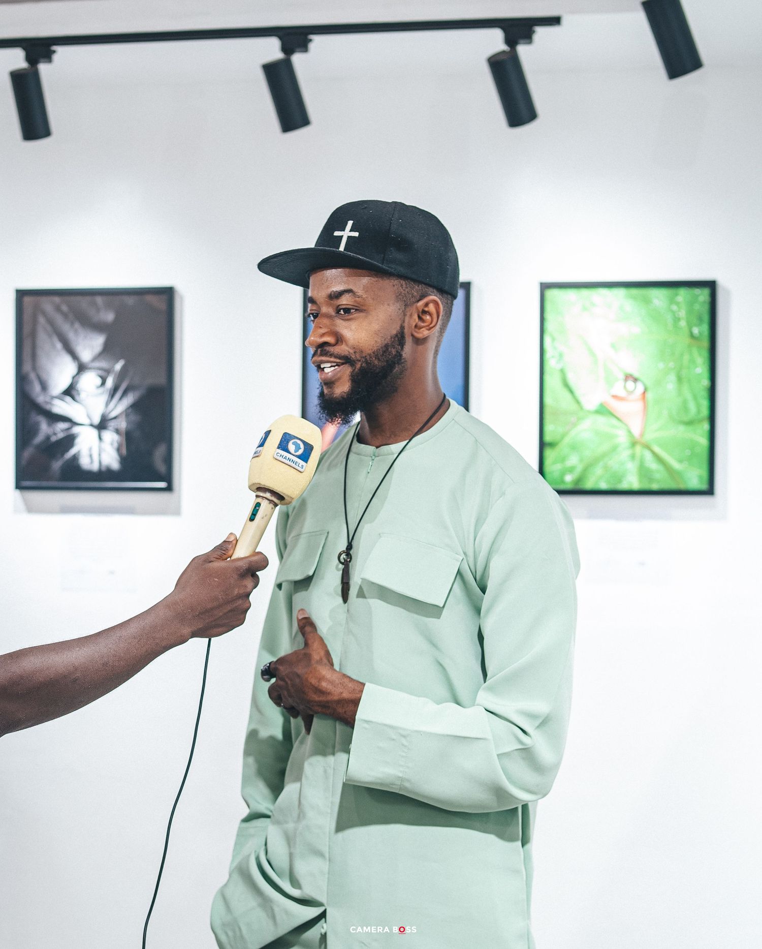 Someone being interviewed by a reporter with a microphone in an art gallery with framed artwork visible on the wall.