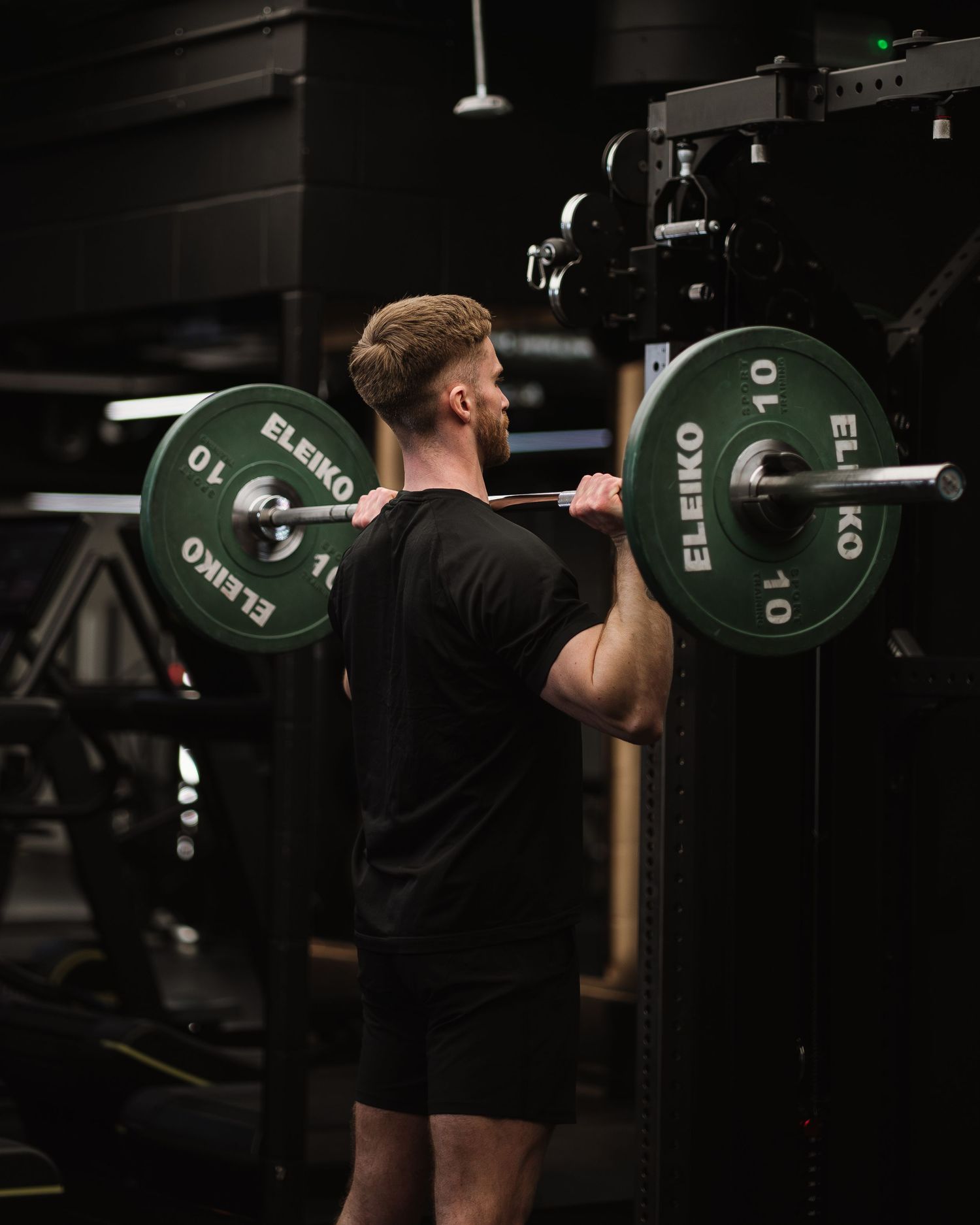 Athlete performing a back squat with a loaded barbell in a dimly lit gym setting.