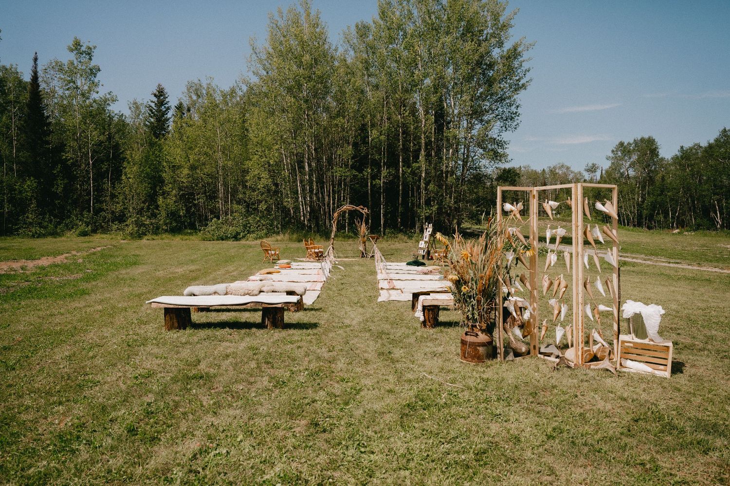 Outdoor wedding ceremony setup with wooden benches and decorative arch in a forest clearing.