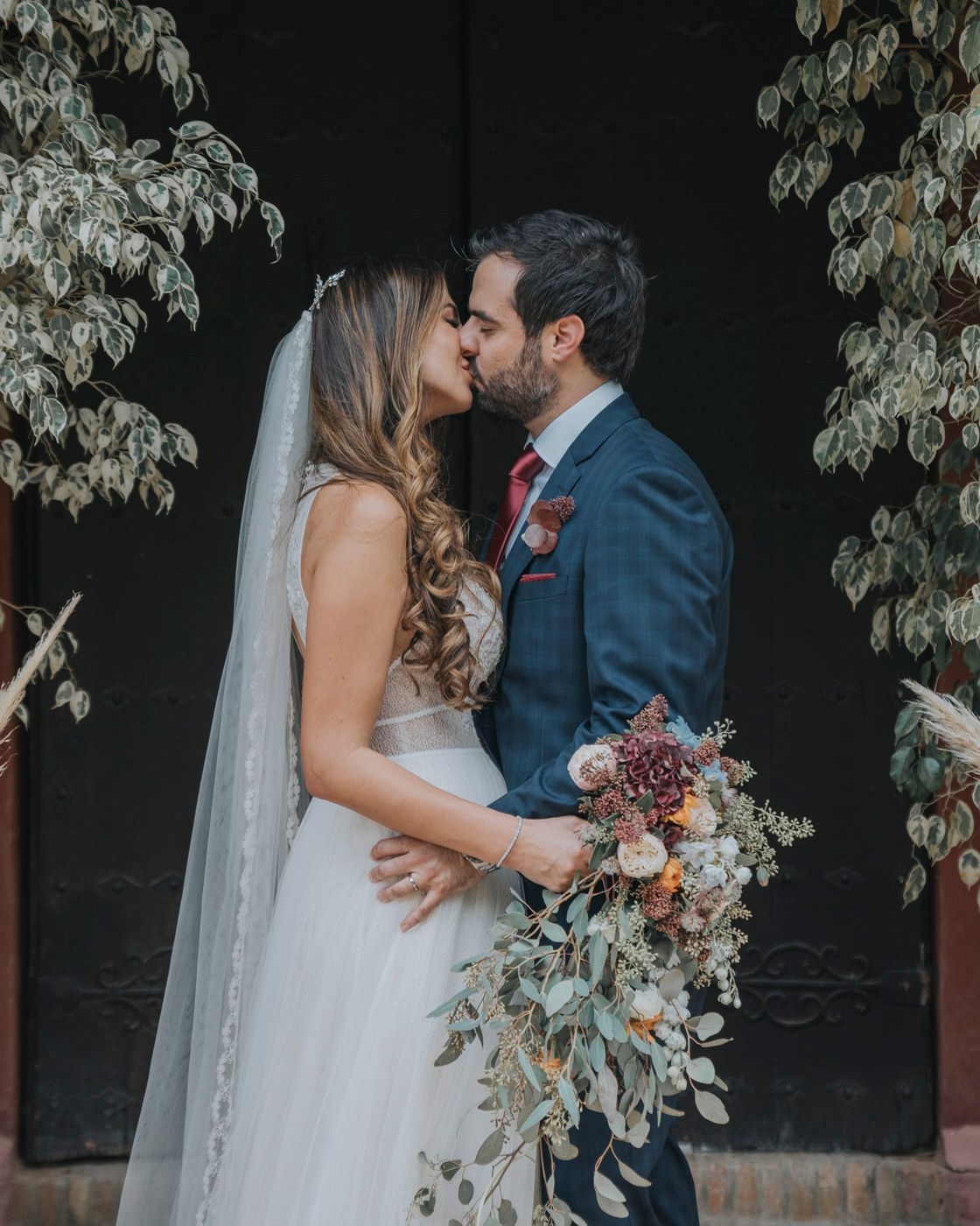 A romantic moment captured between newlyweds under an archway with flowing white bouquet and navy suit.