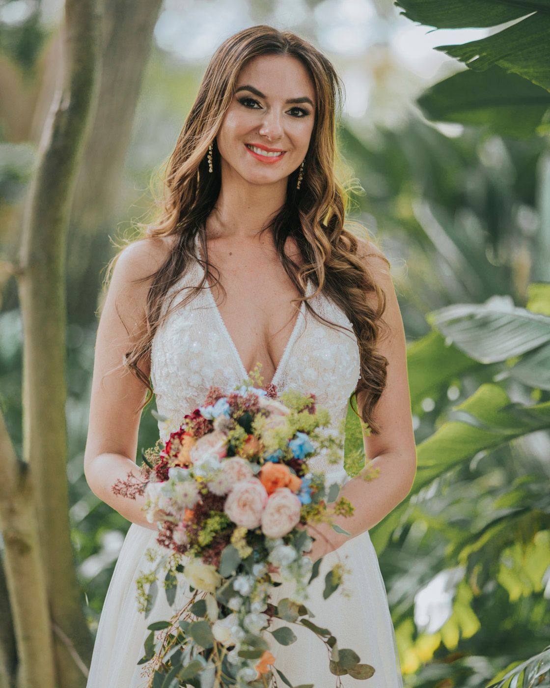 Beautiful wedding portrait showcasing an elegant lace bridal gown and colorful bouquet against a tropical garden backdrop.