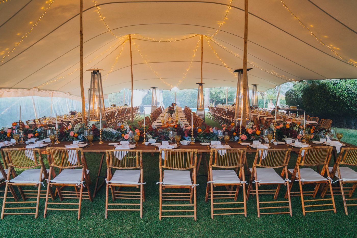 An elegant outdoor wedding reception under a white tent with string lights and wooden chairs set for dinner.