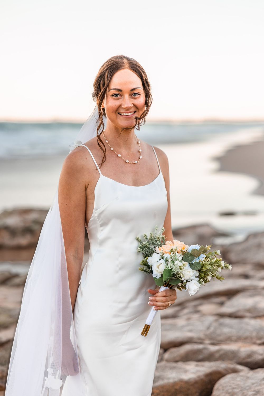 newly married bride Megan holding her bouquet on a Sunshine Coast Beach by the rocks