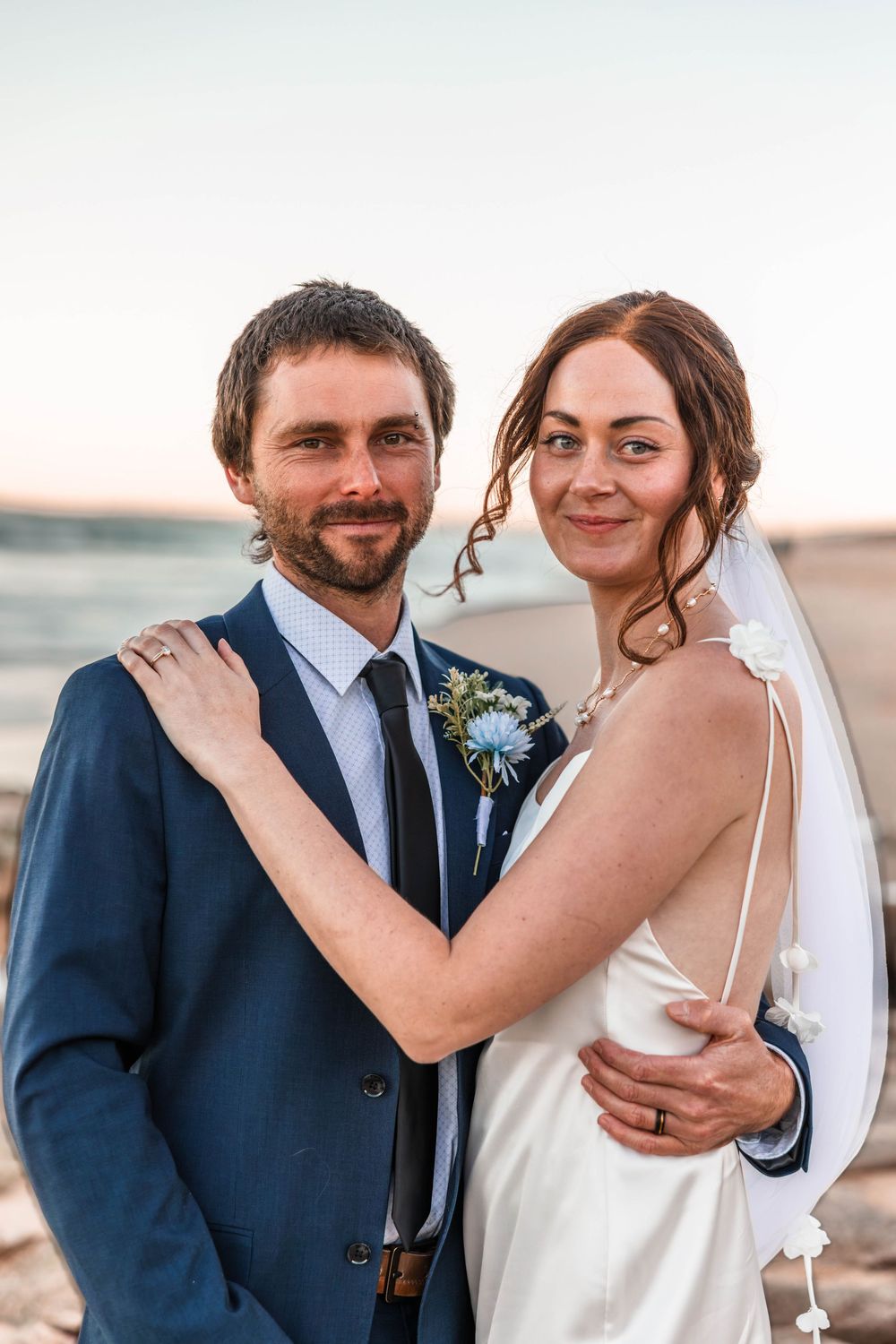 waste up image of nearly married couple Megan and Andy looking at the Camera with Beach for the background