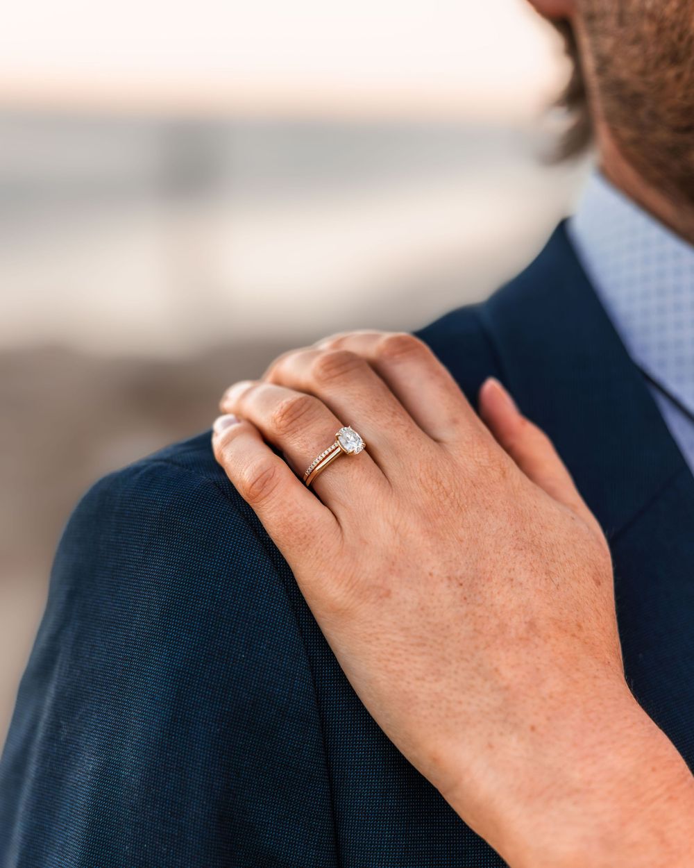 close up of the grooms shoulder with his wife's hand and her wedding ring