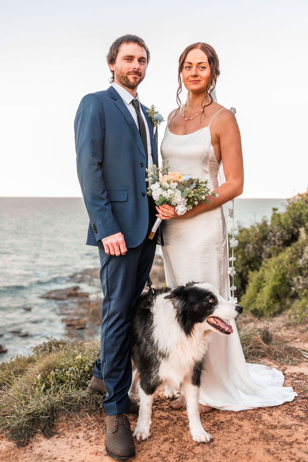 bride and groom standing on a Sunshine Coast Beach Lookout with their dog at their feet