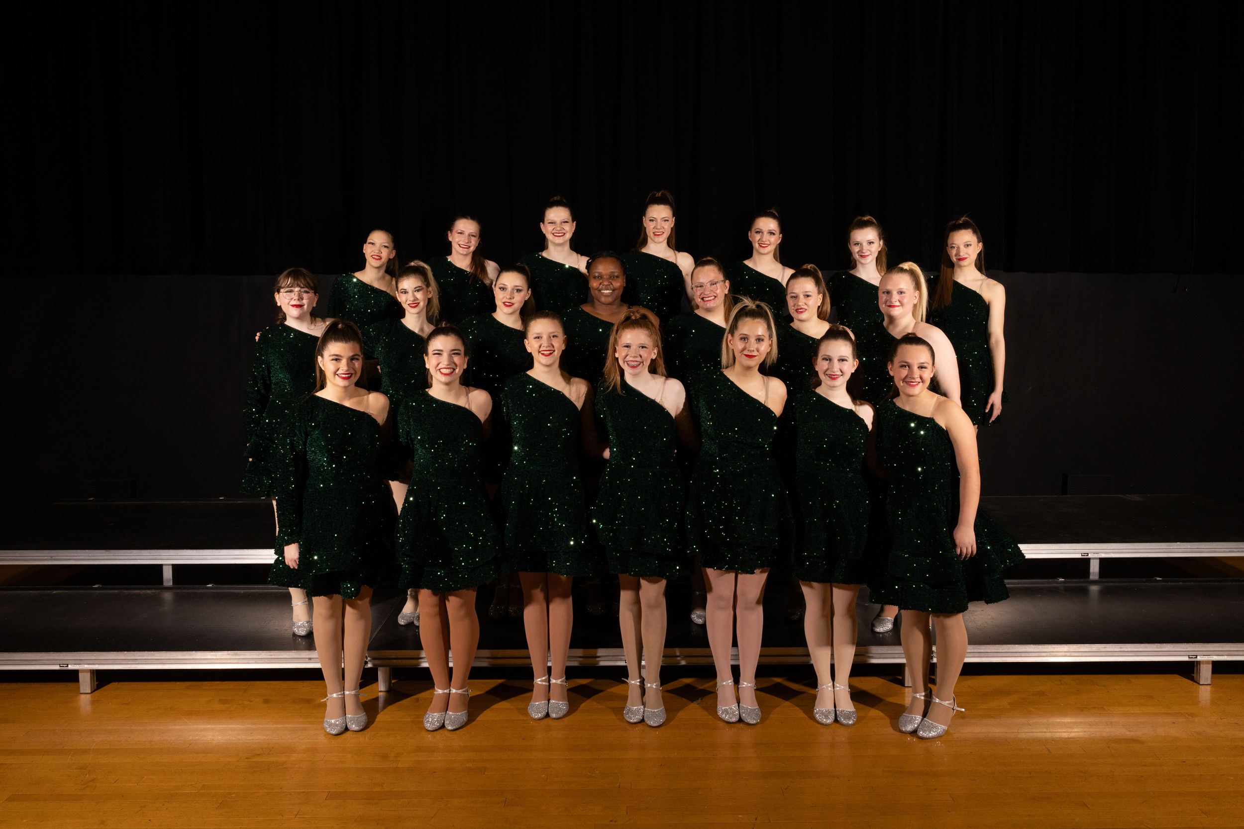 Dance group in black costumes performs synchronized routine on stage.