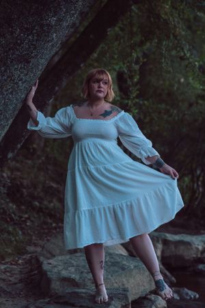 A dreamy portrait of someone in a flowing white dress posing against dark rocks.
