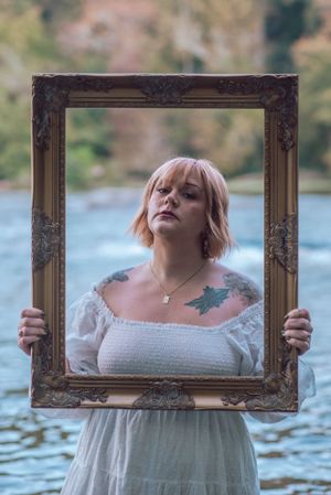 A creative portrait using an ornate frame held up against a waterfront background.