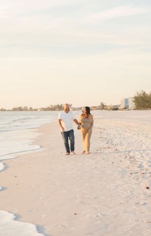 Couple walking together on white sandy beach with coastal buildings in background at dusk.