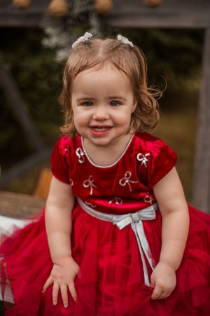 A child in a festive red holiday dress with white bows and silver accents smiles for a series of photos.