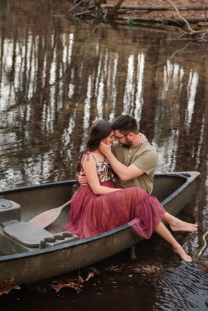 Couple shares tender moment in canoe surrounded by reflective water and winter trees.
