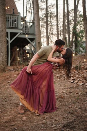 Romantic dip pose near cabin with burgundy dress flowing during sunset.