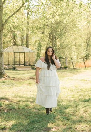 Ethereal white tiered dress photographed in a sunlit garden setting with a greenhouse in the background.