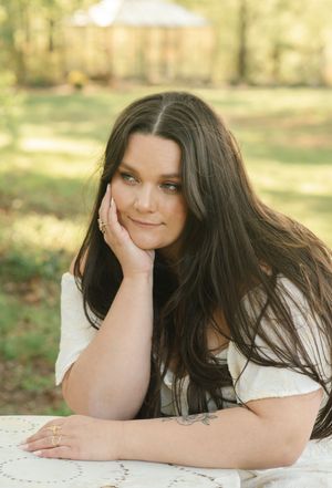 Person in a white top rests head on hand while laying on a white surface in an outdoor autumn setting.