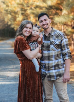 A charming family portrait taken outdoors during autumn with warm earth-toned clothing and fall foliage in the background.