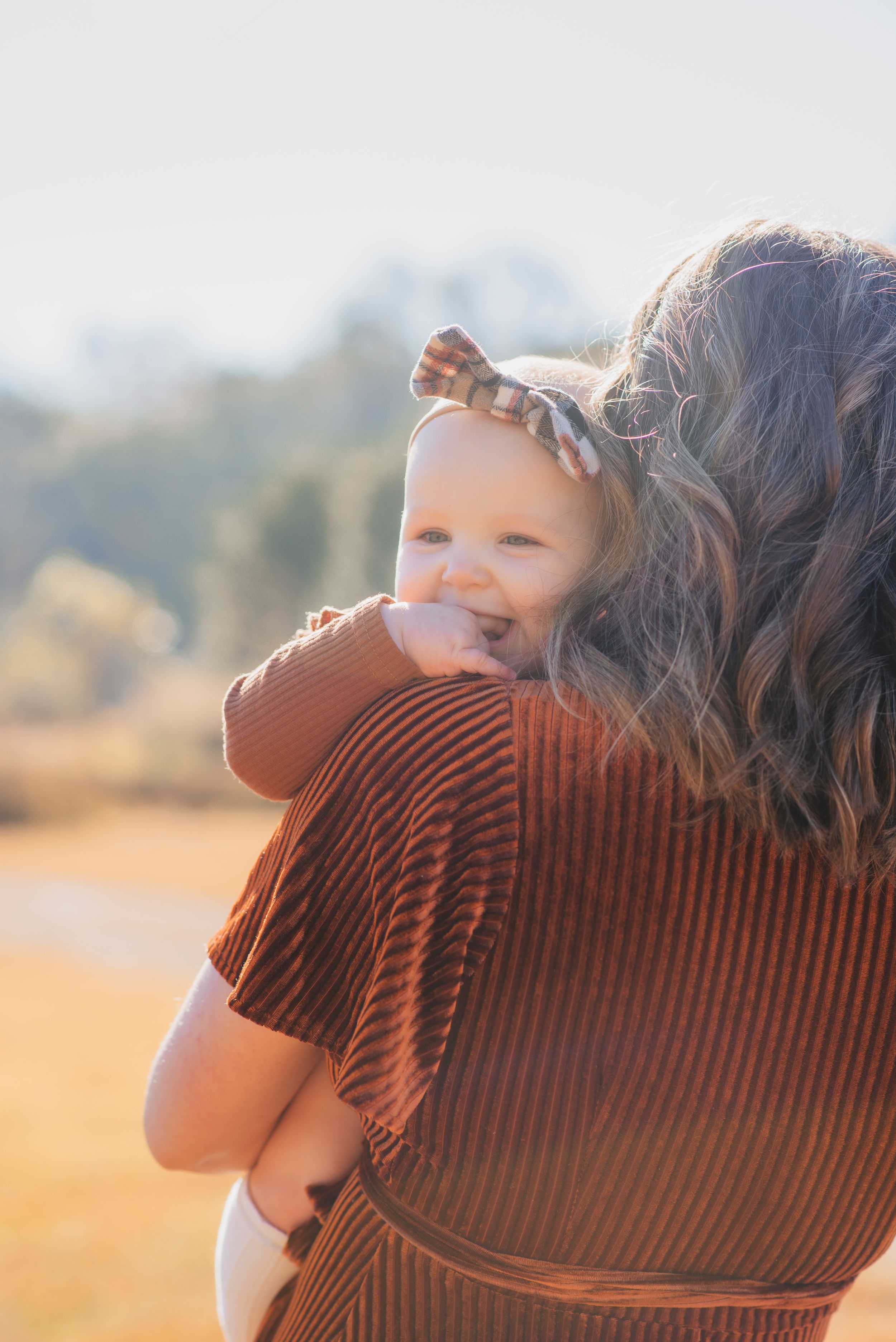 Backlit portrait of parent holding baby during golden hour in autumn setting.