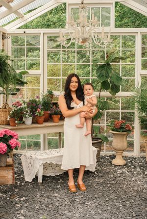 A bright sunlit greenhouse with lush plants, flowering pots, and elegant chandelier creates a serene garden setting.