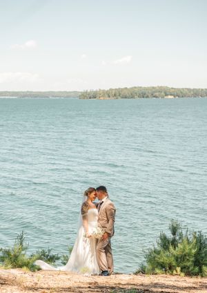 A couple shares an intimate moment on a cliff overlooking a vast blue lake on their wedding day.