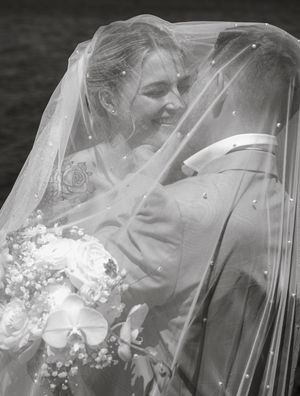 Four black and white wedding photos show a bride behind a veil sitting in a car at different angles.