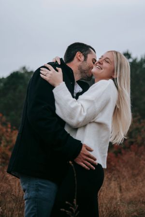 Couple embracing and laughing in warm winter clothing against fall foliage.