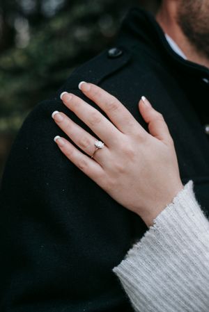 Close-up of a hand wearing a white sweater and engagement ring resting on a black coat.