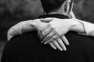 Close-up of hands with engagement ring embracing in black and white.