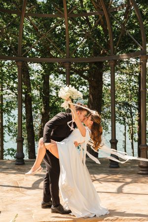 A couple share a romantic dip pose while dancing in a sunlit wooden gazebo surrounded by lush greenery.