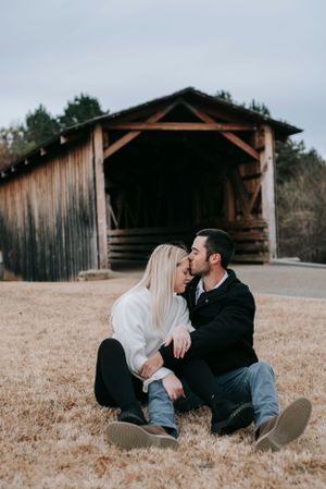Couple sitting together in front of a rustic wooden covered bridge.