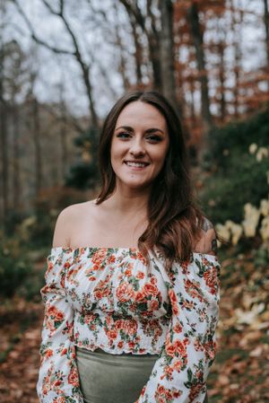 Person in a floral off-shoulder top poses outdoors during autumn.