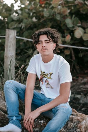 Person wearing white t-shirt and ripped jeans sitting on rocks.