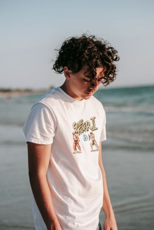 Person in white t-shirt standing by ocean shore at sunset.