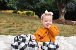 Happy baby in orange sweater plays with black and white plaid decorations.