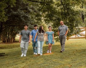 A family of five walks together on a grassy hill during a sunny summer day in the park.