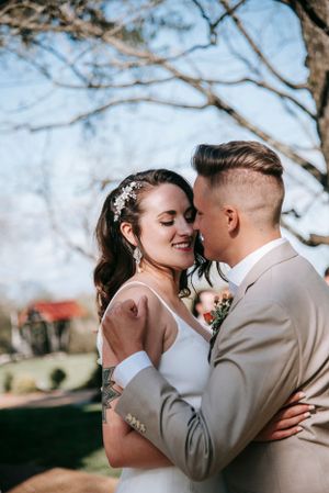 A romantic wedding couple embracing outdoors, with the bride in white and groom in beige.