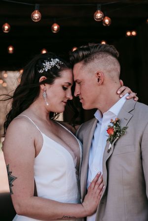 A romantic wedding portrait under string lights with the couple in classic white and beige attire.