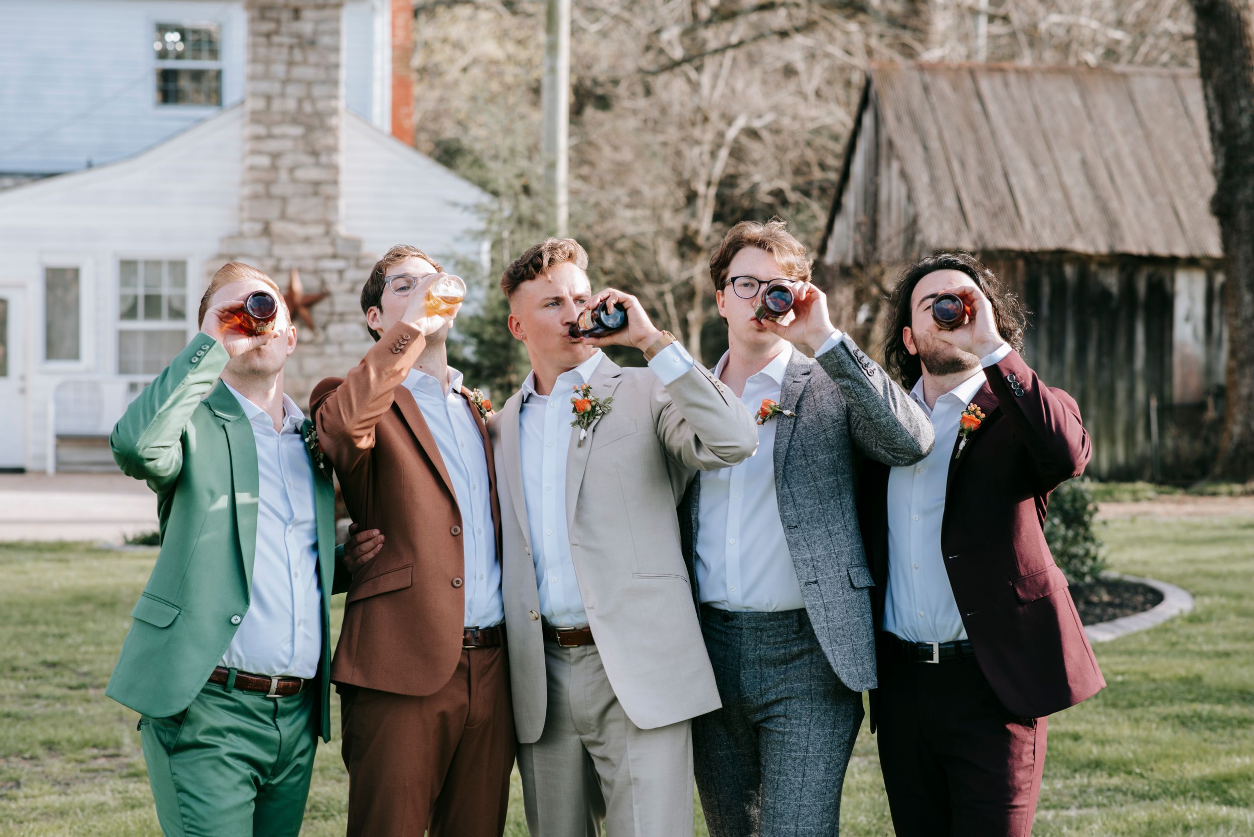 Five groomsmen in colorful suits pose together making exaggerated laughing expressions.