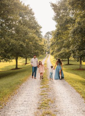 A family walks together on a gravel path through an orchard on a sunny autumn afternoon.