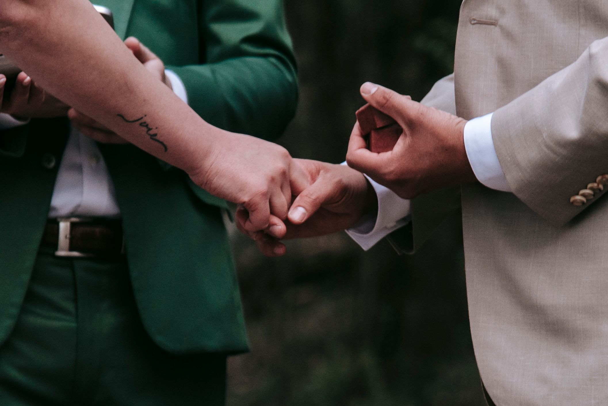 Close-up of two people holding hands wearing contrasting green and beige formal attire.