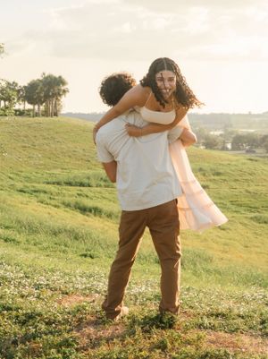 Playful piggyback ride moment captured on grassy hillside during sunset.